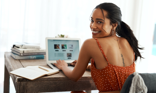 Woman smiling while using laptop at wooden table.